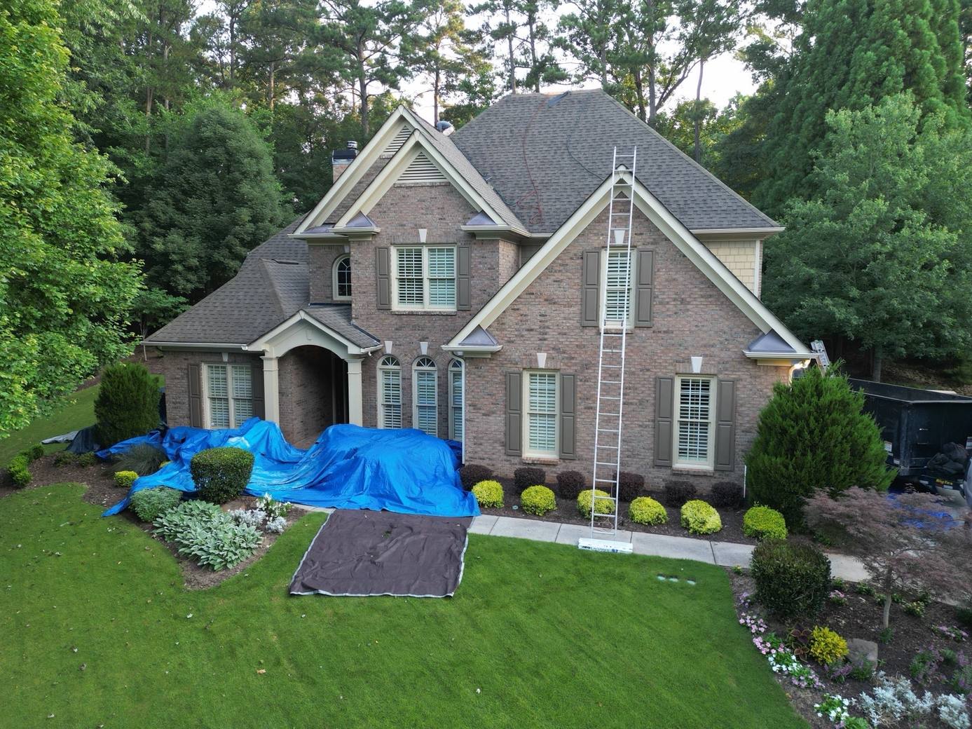 Two-story brick home in Suwanee GA with tarps over the landscaping before the old shingle roof was torn off