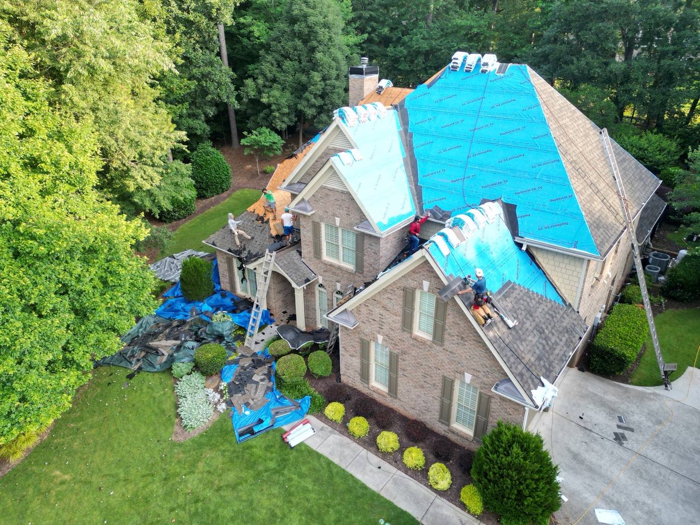 Crew installing new architectural shingles over blue underlayment on a two-story brick house in Suwanee GA